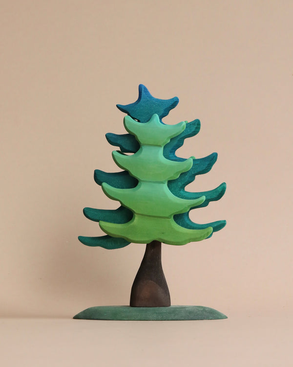 A colorful handmade Extra Large Wooden Green Spruce Tree sculpture with layered green and blue branches on a beige background.