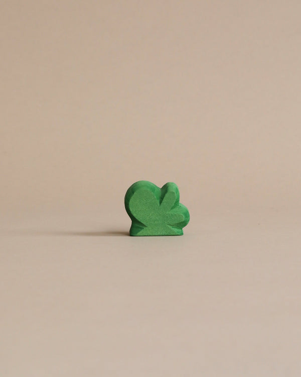 A small green wooden bush, painted with non-toxic paint, standing upright against a light beige background.