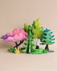 A colorful collection of handmade Japanese Maple Trees crafted from linden wood in different shapes and hues, including pink, green, and blue, artistically arranged against a pale background.