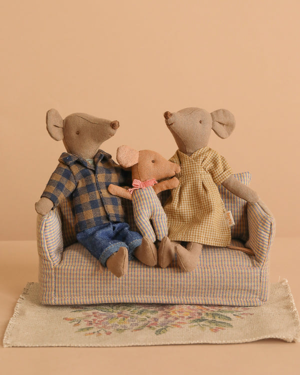 The Maileg Family Set features three charming mouse dolls in plaid outfits sitting on a striped couch atop a floral rug, making them perfect children's toys to brighten up any dollhouse.