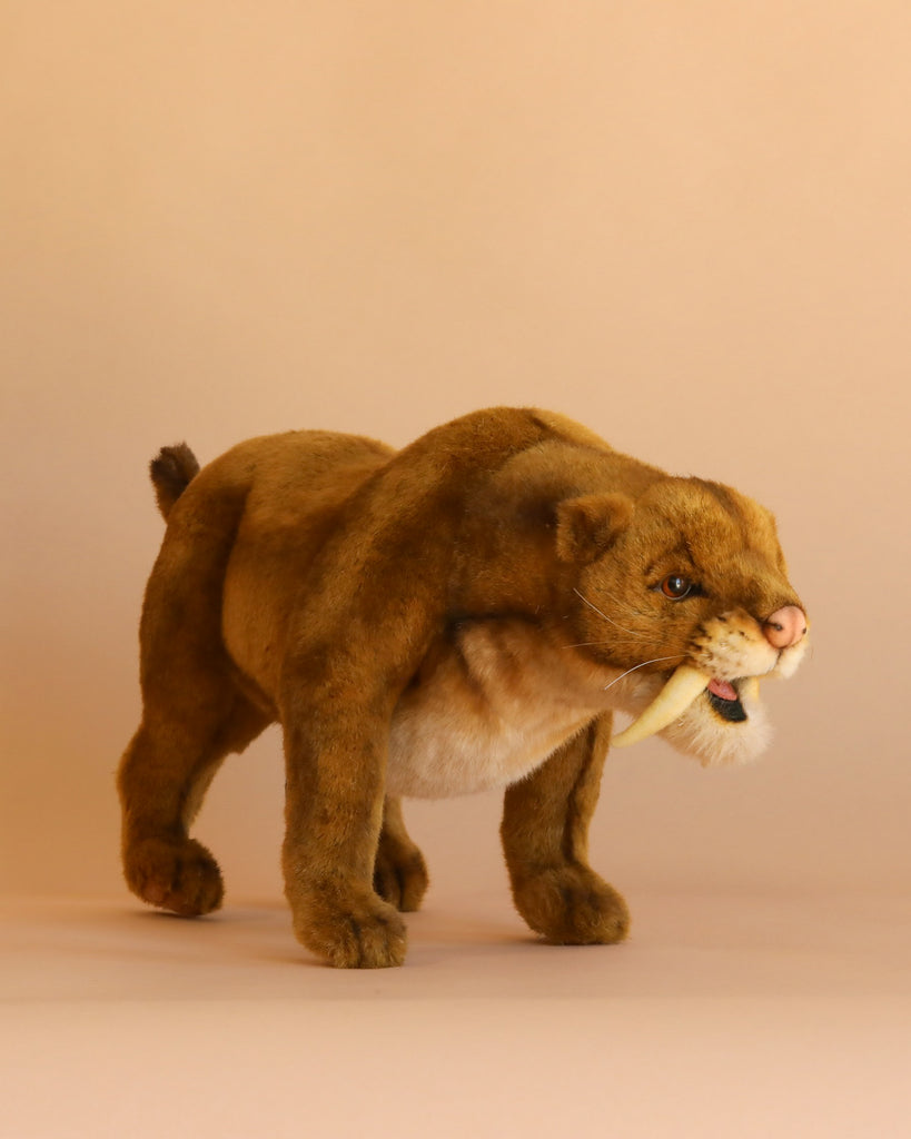 The Saber Tooth Tiger Stuffed Animal, featuring brown fur and large curved fangs, stands on a plain beige background—showcasing the lifelike detail typical of artisan handmade toys and realistic plush animals.