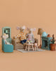 Three toy mice enjoy the Maileg Family Time Living Room Set, featuring mouse dollhouse furniture, a tea set, teal shelves, and a potted plant—all arranged in a cozy scene against a plain peach background.