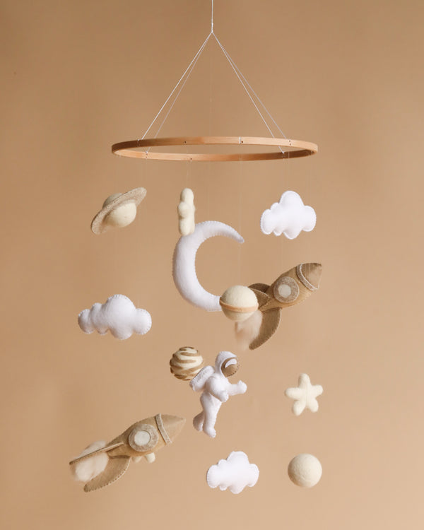 A Handmade Mobile - Among the Stars - Final Sale featuring felt planets, rockets, stars, and clouds in soft beige tones against a warm beige background.