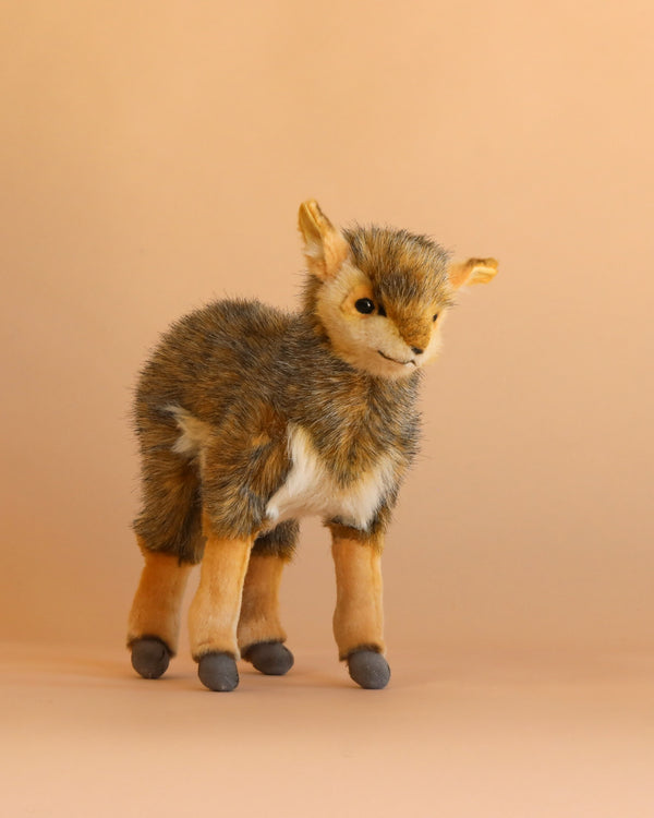 An Antelope Stuffed Animal stands upright on a light tan background. Expertly crafted in the style of handmade plush animals, this toy features soft brown, tan, and white fur with gray hooves and a small smile on its face.