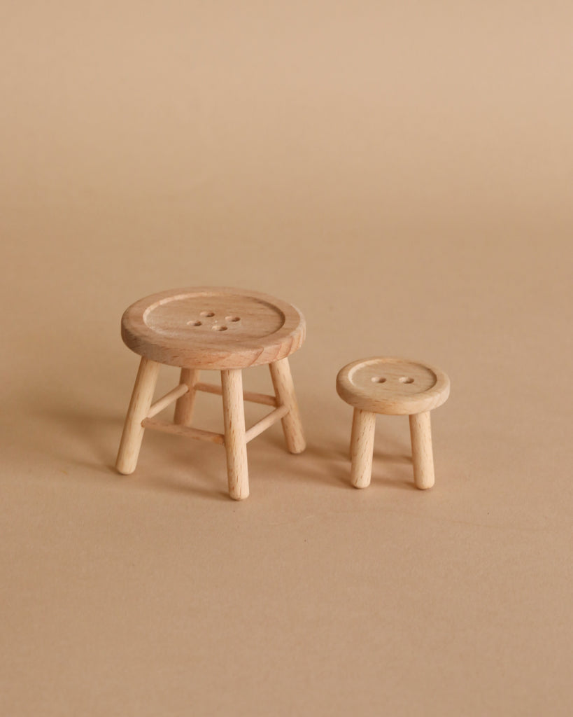 The Maileg Little Sister Bathroom Set features two small wooden stools—one larger than the other—with round button-like seats and three legs each, perfect as dollhouse furniture and shown against a beige background.
