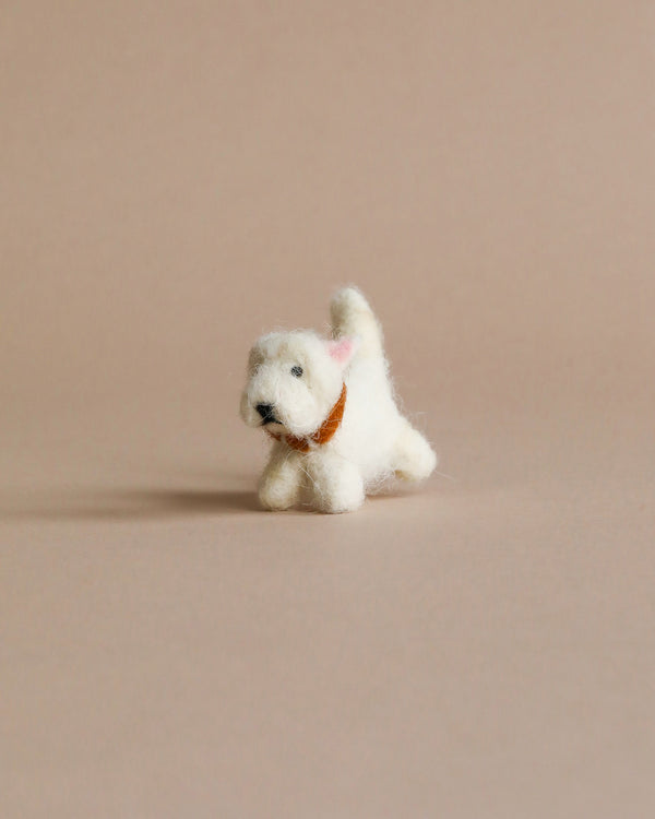 A small, white organic Felt Westie Dog, with a black nose and a tiny brown collar, positioned in a playful stance on a plain beige background.