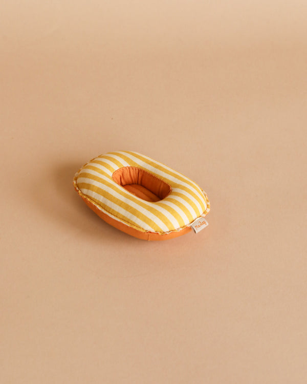 A small, oval-shaped, yellow and white striped Maileg Beach Raft, Small Mouse - Yellow Stripe with an orange underside sits on a plain beige background, resembling a tiny raft. It has a small fabric tag on one side.