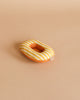 A small, oval-shaped, yellow and white striped Maileg Beach Raft, Small Mouse - Yellow Stripe with an orange underside sits on a plain beige background, resembling a tiny raft. It has a small fabric tag on one side.