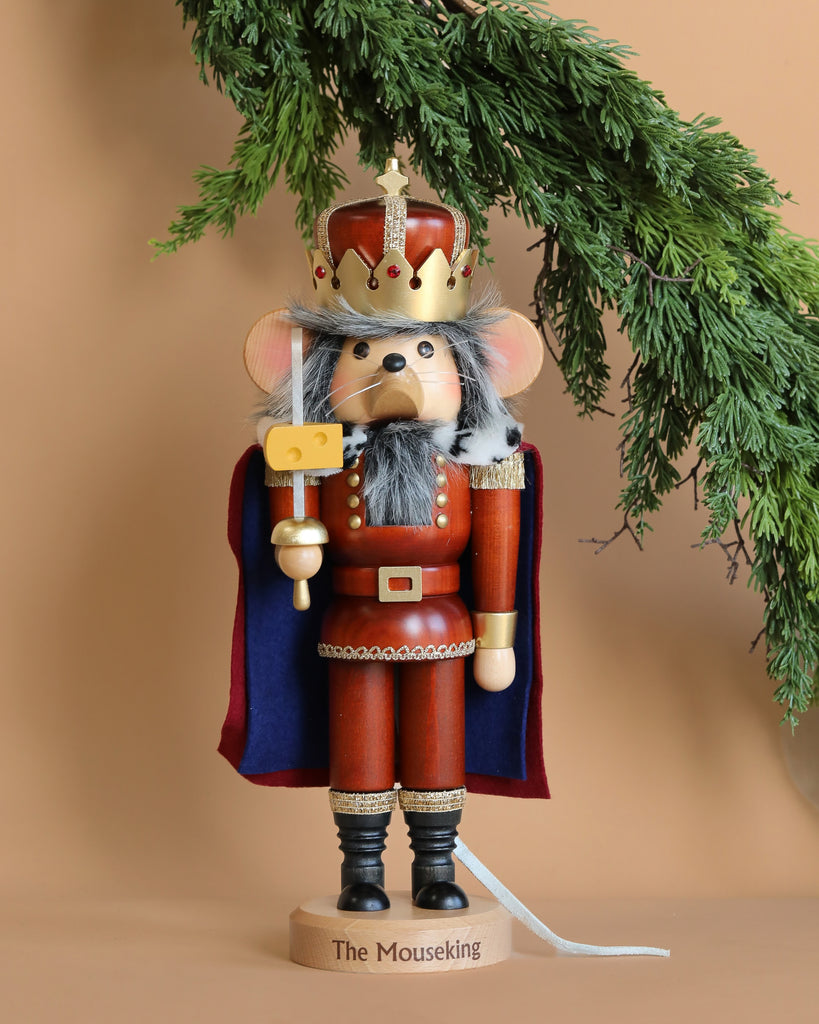 The Christian Ulbricht Collectible Wooden Nutcracker - Mouse King is a limited-edition piece crafted to resemble a regal mouse king, complete with a crown, sword, and cape. Set against a tan background with evergreen branches enhancing its festive appeal, this exquisite nutcracker is made in Germany and embodies timeless holiday tradition.