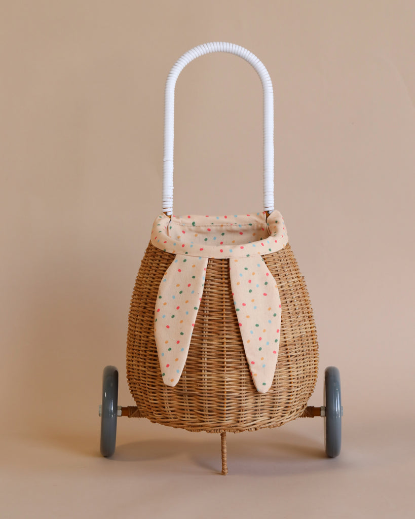 A Rattan Bunny Luggy With Lining – Gumdrop on wheels with a white handle, decorated with a fabric liner featuring a polka dot design, displayed against a neutral backdrop.