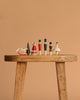 A wooden stool displays Sabo Concept Wooden Nutcracker Figurines—two soldiers—plus a handmade rocking horse, tree, bear, man, and ballerina, all neatly arranged in a row against a simple beige background.