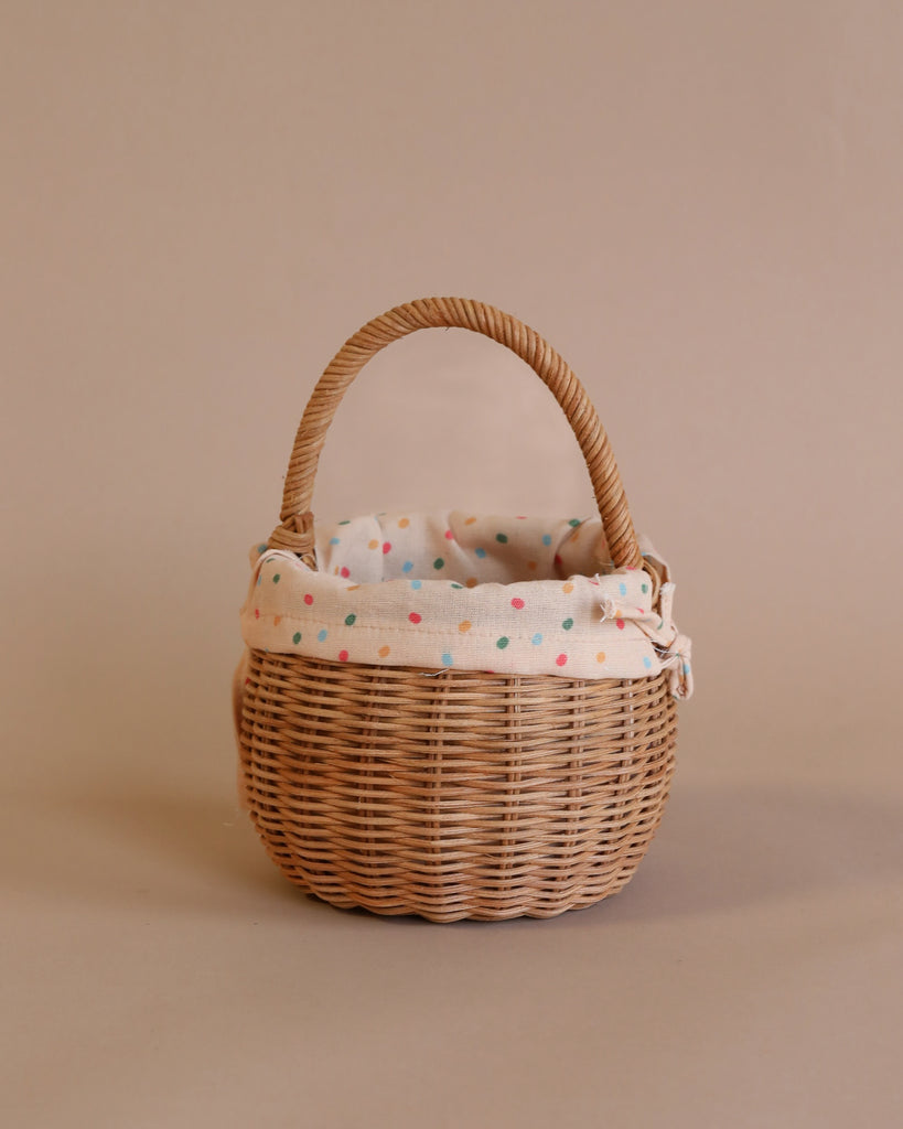 A handmade rattan berry basket with a handle, lined with a white fabric featuring multicolored polka dots, set against a plain beige background.