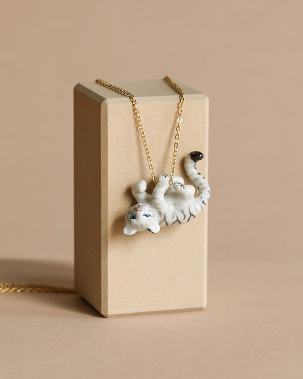 A White Tiger Cub Necklace with a sloth pendant hanging on a 24k gold plated chain, displayed on a beige cardboard box against a matching beige background.