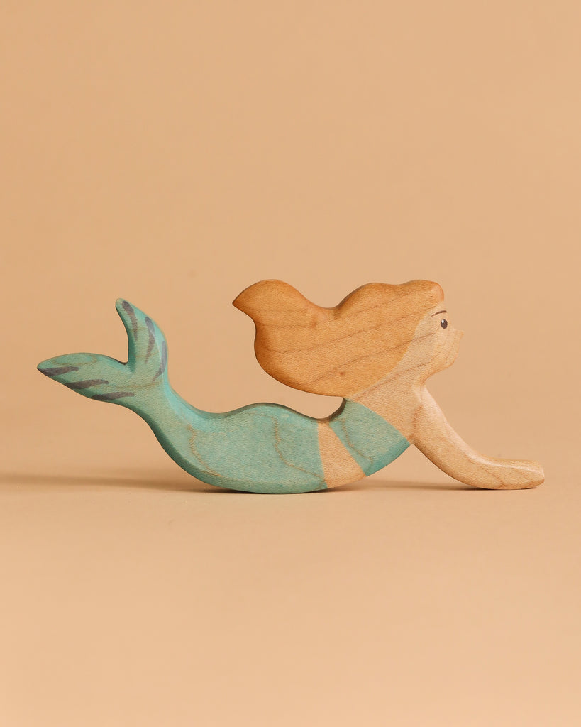 The Handmade Holzwald Mermaid features light brown hair and a greenish-blue tail, posed as if swimming against a plain beige background—perfect for inspiring open-ended play.