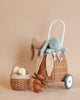 A charming still life featuring a small natural Rattan Bunny Luggy With Lining – Gumdrop, adorned with plush toys, including a blue and a brown bunny. Next to it, a smaller handmade