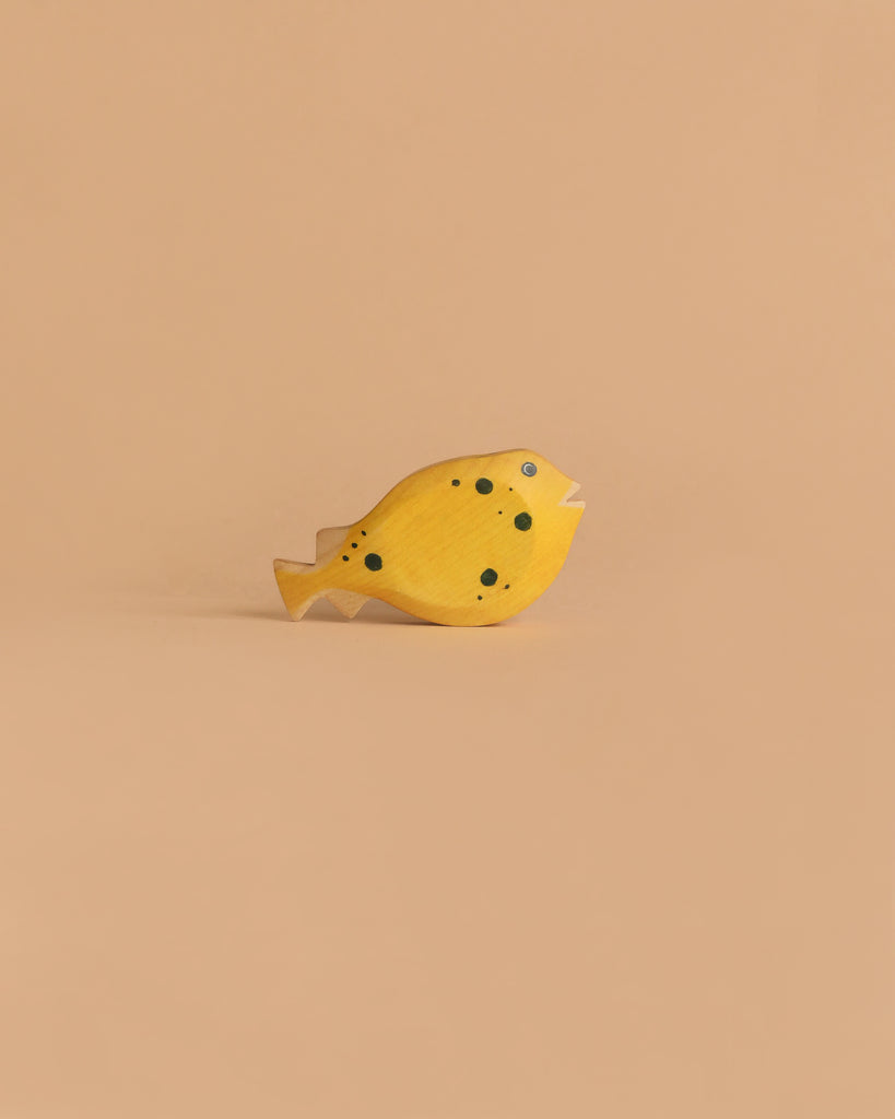 The Handmade Holzwald Pufferfish is a small, yellow wooden toy with black spots and a simple design, displayed on a light brown background—a charming example of sustainable craftsmanship.