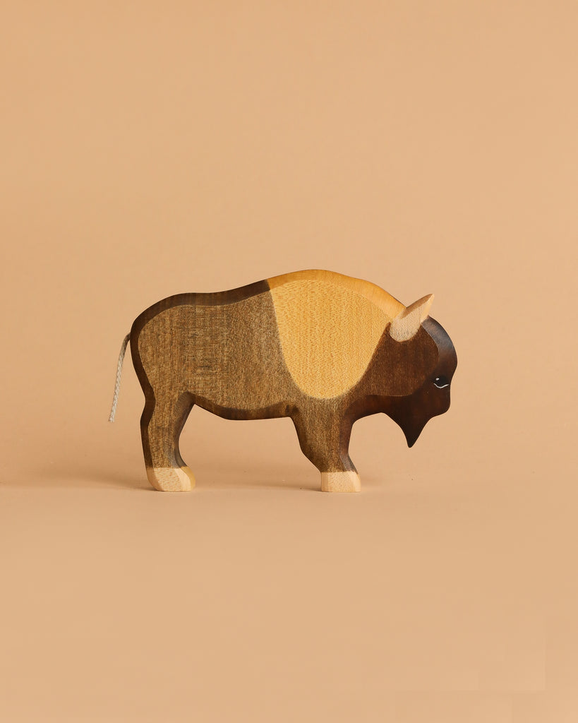 The Handmade Holzwald Bison, a wooden figurine with natural wood colors and distinct dark brown, tan, and light sections, stands on a beige background—perfect for educational and sustainable toy enthusiasts.