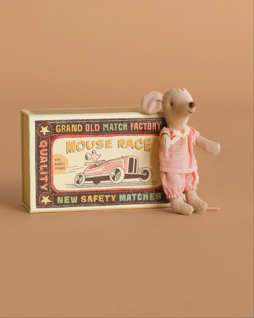 The Maileg Little Sister Mini House Set features a mouse in pink gingham beside a decorative “Mouse Race” matchbox with a vintage race car illustration on a tan background.