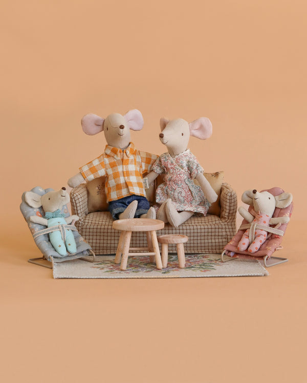 The Maileg Family Living Room Set features two adult and two child mice arranged on a couch and Maileg mouse furniture, creating a charming family scene against a plain peach background.