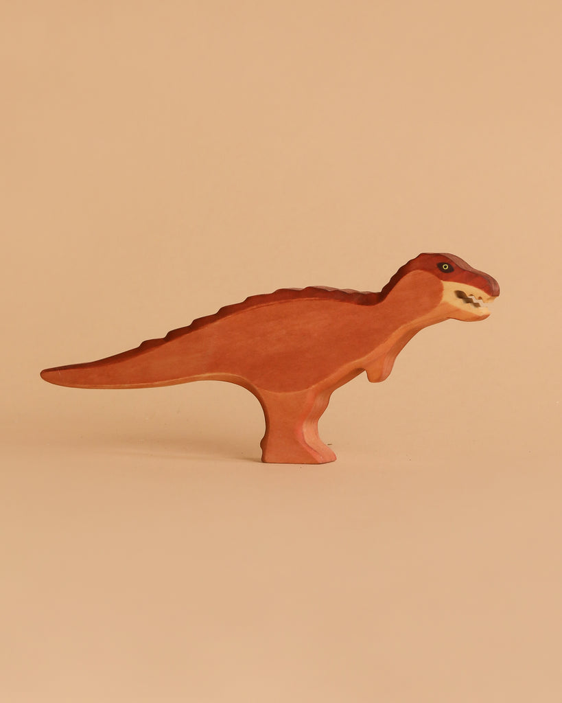 The Handmade Holzwald T-Rex Maroon, a sustainable wooden dinosaur figurine, stands upright on a light beige background. Painted in maroon and brown with green eyes and white teeth, it features a slightly open mouth.