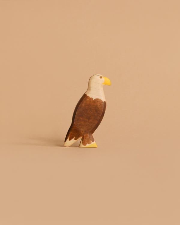 The Handmade Holzwald Eagle is a wooden figurine featuring a yellow beak and brown and white painted details, standing upright—perfect for any collection of sustainable wooden toys.