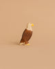 The Handmade Holzwald Eagle is a wooden figurine featuring a yellow beak and brown and white painted details, standing upright—perfect for any collection of sustainable wooden toys.