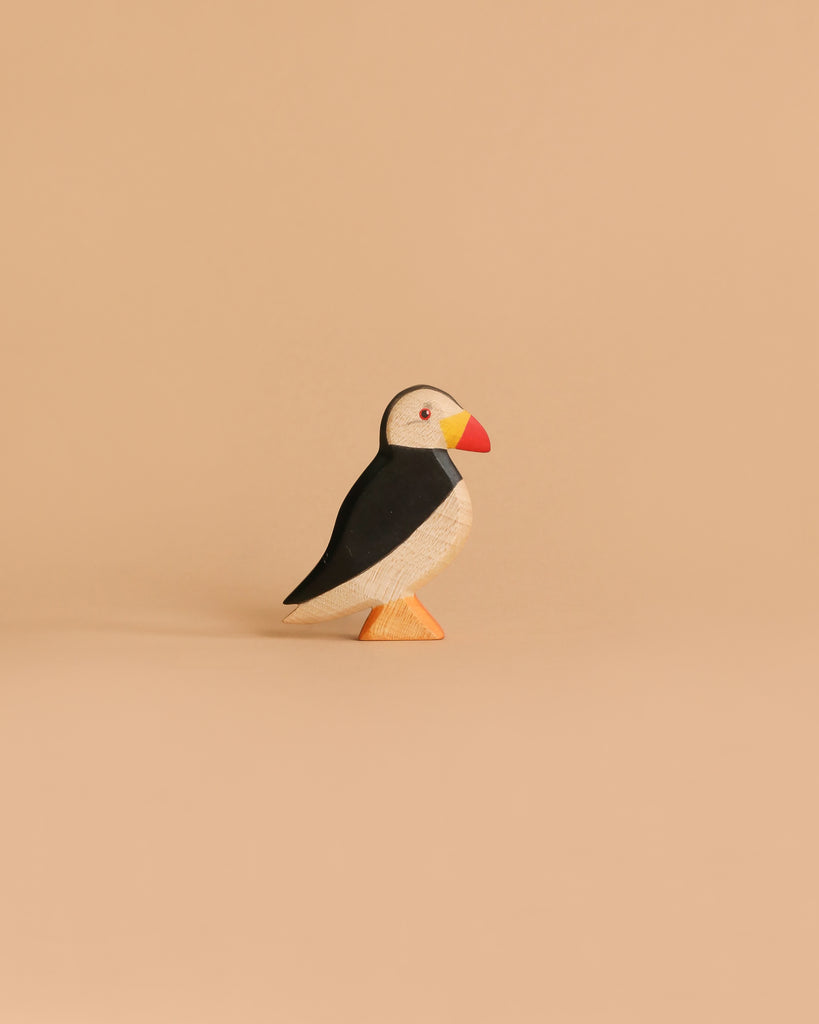 The Handmade Holzwald Puffin Bird is a small wooden toy with black, white, and orange details, standing upright on a beige background—a charming example of sustainable craftsmanship.