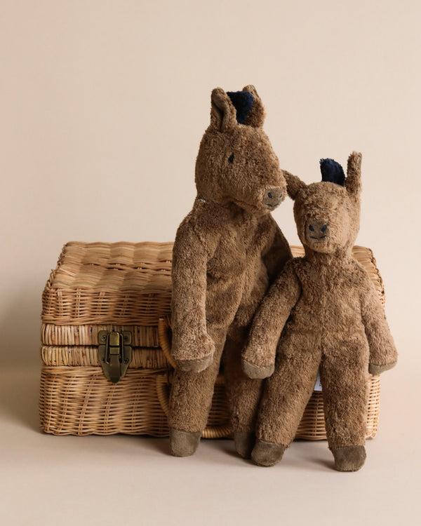 Two Senger Naturwelt Stuffed Animal - Horse toys, one larger and one smaller, leaning against a woven wicker basket with a latch on a neutral background. These handmade toys enhance the charm of the setting.