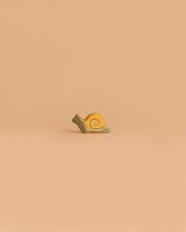 The Handmade Holzwald Small Snail, a delightful yellow toy with a spiral shell, rests on a flat surface against a plain beige background—perfect for inspiring imaginative play and appealing to creative minds.