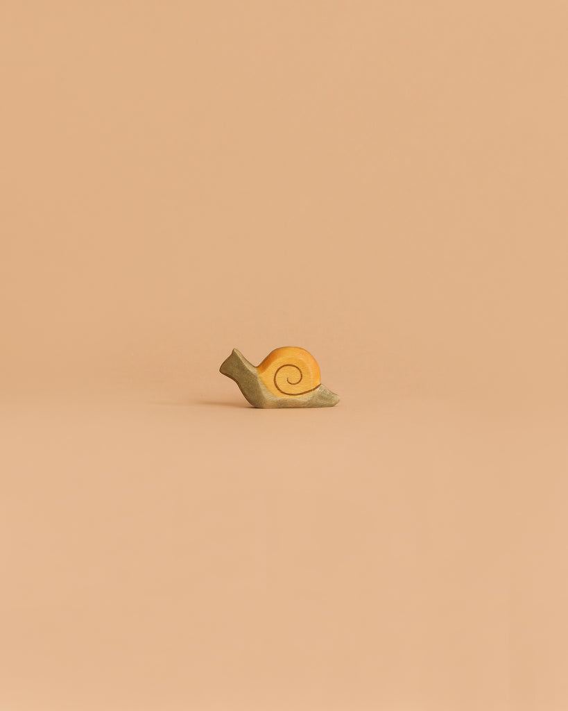 The Handmade Holzwald Small Snail, a delightful yellow toy with a spiral shell, rests on a flat surface against a plain beige background—perfect for inspiring imaginative play and appealing to creative minds.