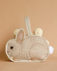 A whimsical children's handbag shaped like a Coral & Tusk Bunny Basket, with an embroidered bunny design, accompanied by a small plush duck peeking from behind, against a light brown background.