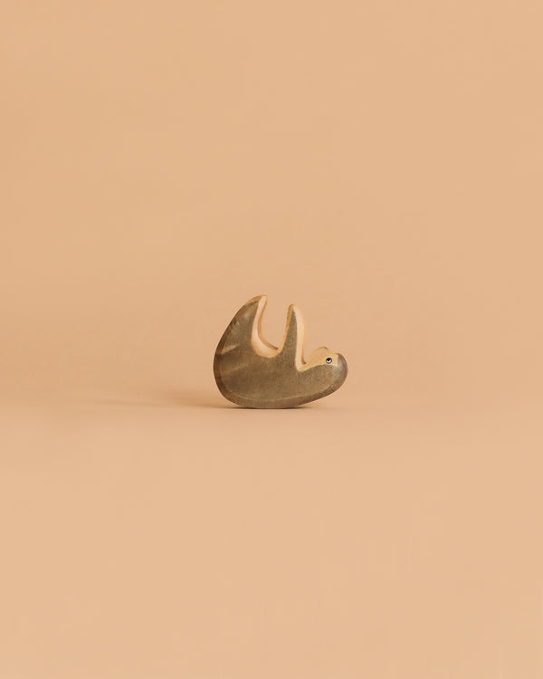 The Handmade Holzwald Small Sloth, a small wooden toy with a simple design, lies on its back against a plain light beige background—a delightful addition to any sustainable toy collection.