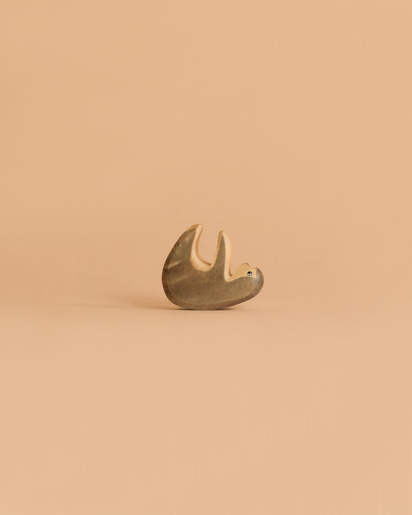 The Handmade Holzwald Small Sloth, a small wooden toy with a simple design, lies on its back against a plain light beige background—a delightful addition to any sustainable toy collection.