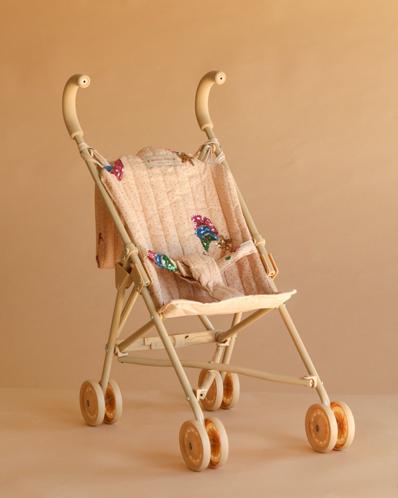 The Konges Sloejd Tulle Doll Stroller - Rainbow Star features a quilted beige seat adorned with colorful rainbow star patterns, curved handles, and four pairs of double wheels with yellow accents, all set against a plain beige background.