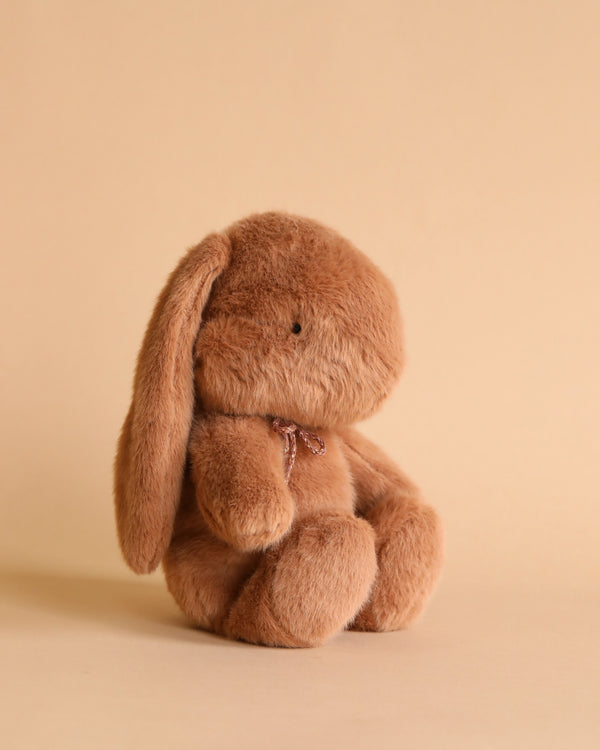 Brown plush bunny with bow around its neck. Photographed against beige background. 