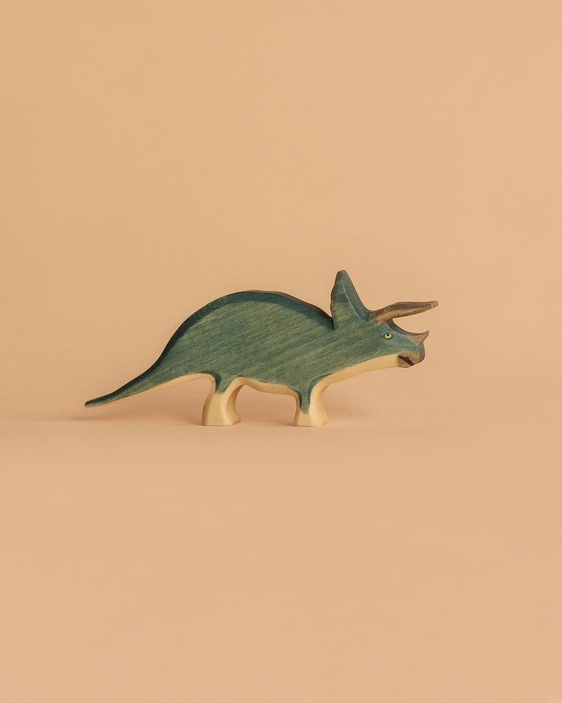 Part of the Handmade Holzwald Dinosaur Set, this blue and cream wooden triceratops stands on a beige background—ideal for lovers of sustainable wooden toys.