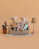 The Maileg Family Living Room Set features four dressed mice on a small couch, with a potted plant, a beige flower rug, and a patterned lamp, all set against a light brown background.