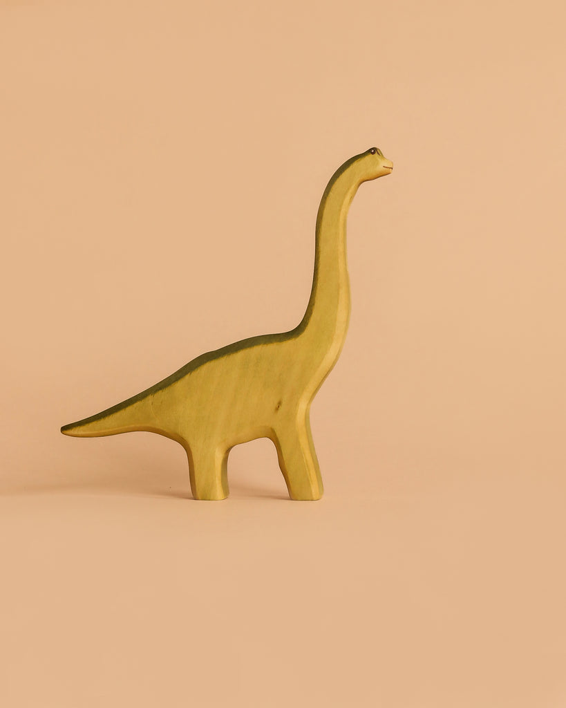 A yellow dinosaur from the Handmade Holzwald Dinosaur Set, crafted from wood and resembling a brontosaurus, stands on a simple peach background.