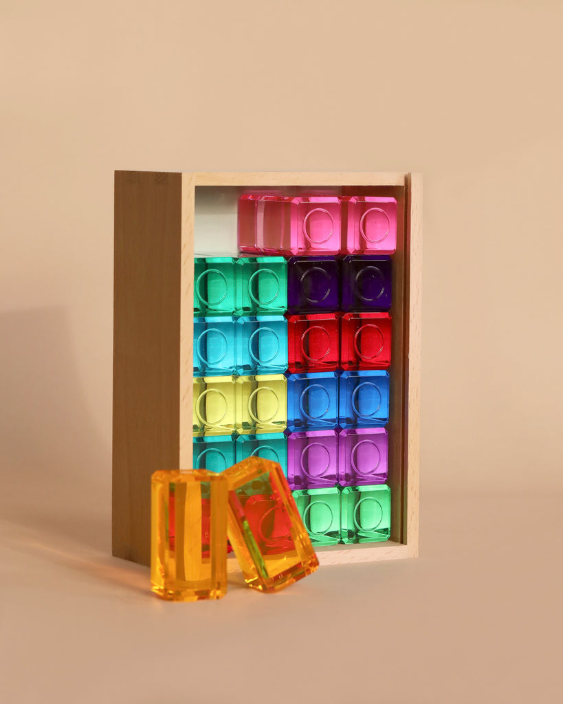 The Bauspiel Luminous Blocks - 24 Piece set is a high-quality wooden toy featuring colorful translucent blocks in a grid. Two orange blocks stand out against a neutral background, perfect for endless educational building adventures.