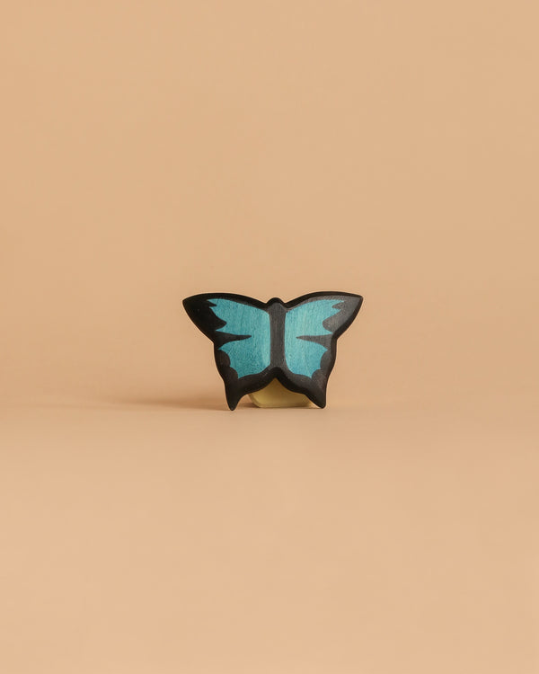 The Handmade Holzwald Butterfly, a small decorative blue and black figurine, is centered on a plain light beige background—an elegant example of sustainable toys.