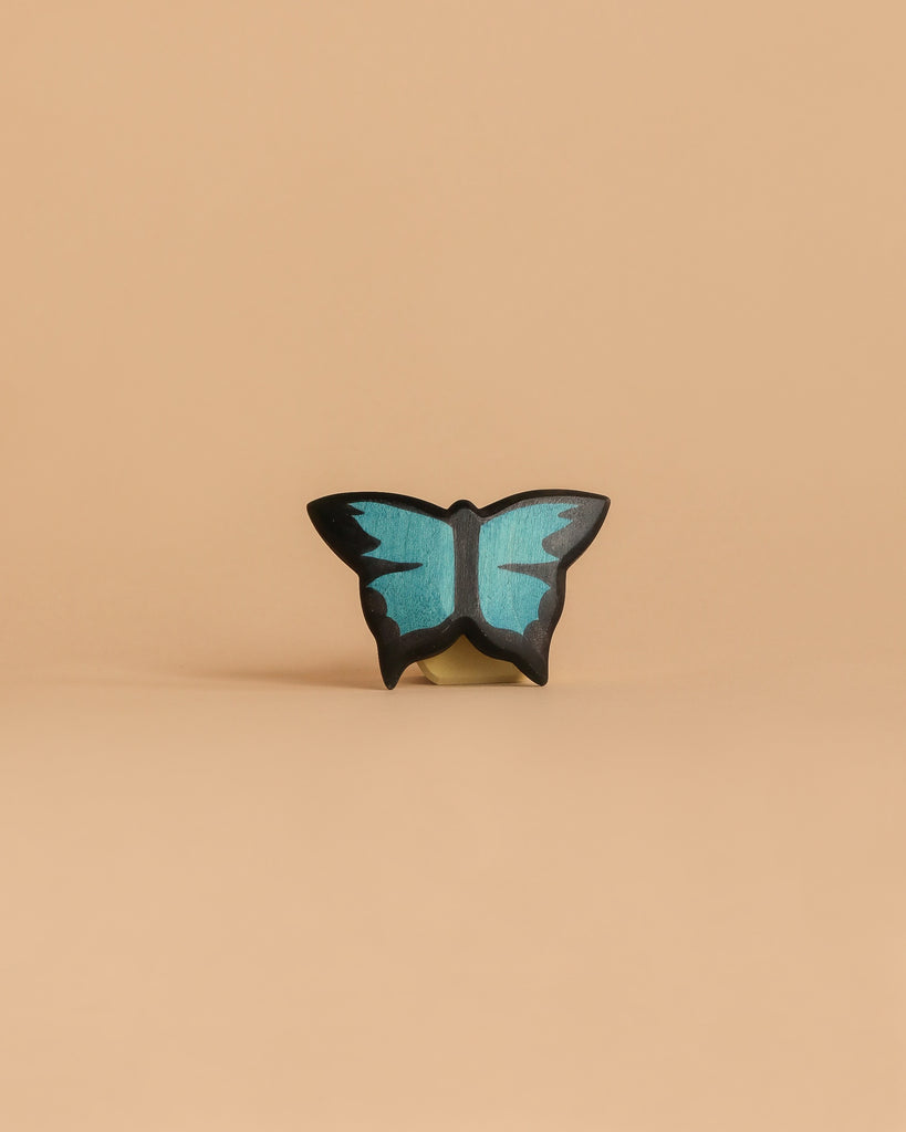 The Handmade Holzwald Butterfly, a small decorative blue and black figurine, is centered on a plain light beige background—an elegant example of sustainable toys.