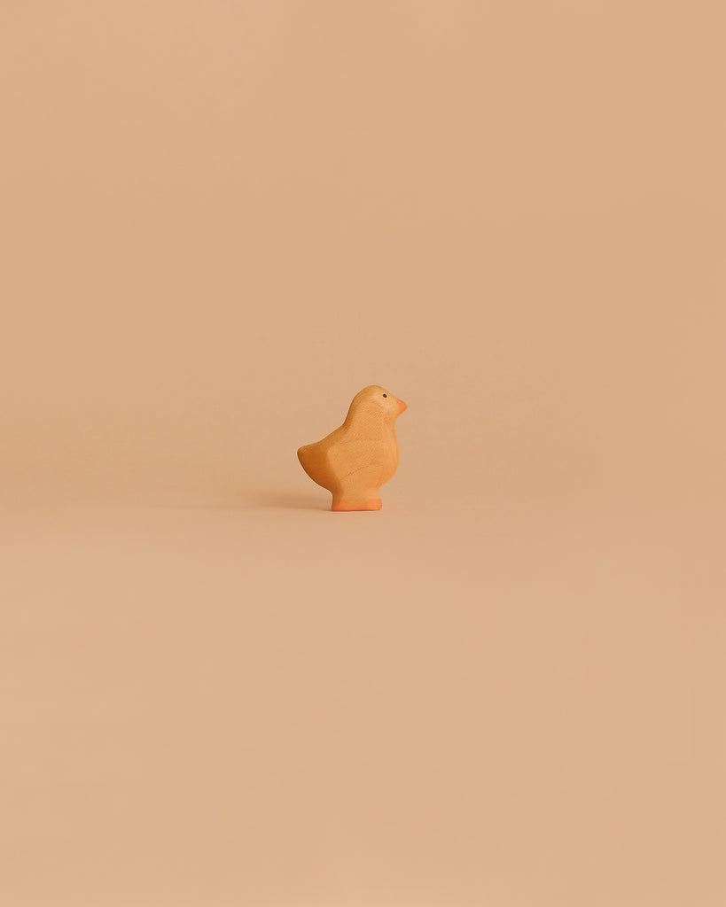 The Handmade Holzwald Baby Chick, a small wooden figurine with an orange beak and base, stands alone on a light beige background—an ideal pick for anyone seeking sustainable or unique wooden toys.