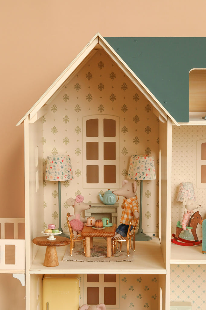 The Maileg Fully Furnished Dollhouse Set + Surprise Gift includes two toy mice at a table, tea set, floral wallpaper, lamps, and miniature furniture—creating a cozy space perfect for imaginative play.