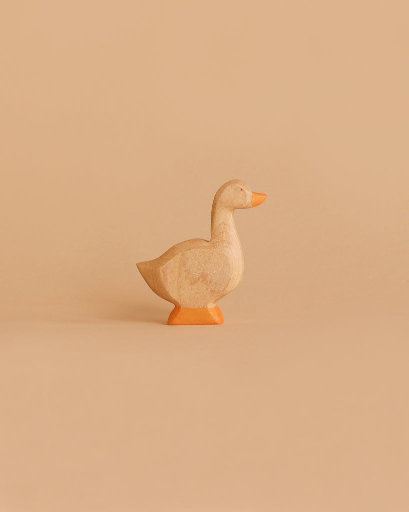 A small, Handmade Holzwald Goose with an orange beak and base stands against a plain, light tan background—perfect for those who appreciate sustainable toys.