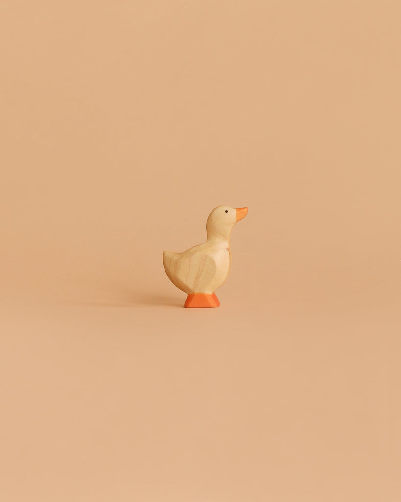 The Handmade Holzwald Gosling, a small wooden toy duck with orange beak and feet, stands on a light beige background—ideal for imaginative play and a delightful addition to any sustainable toy collection.