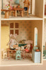 Two toy mice, dressed in clothes, sit at a kitchen table inside the Maileg Fully Furnished Dollhouse Set + Surprise Gift, featuring mini furniture like a yellow fridge, stove, cabinets, and playful household items for a cozy scene.