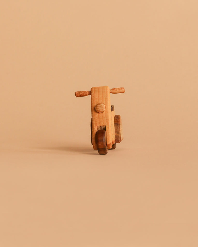 The Handmade Wooden Scooter, crafted from beech wood with a minimalist design, stands upright on a light brown surface against a matching brown background.