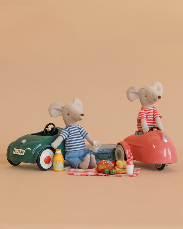 The Maileg Big Brother and Sister Adventure Extended Set features two mice in striped shirts enjoying a picnic with toy food beside green and pink toy cars, all against a plain beige background.