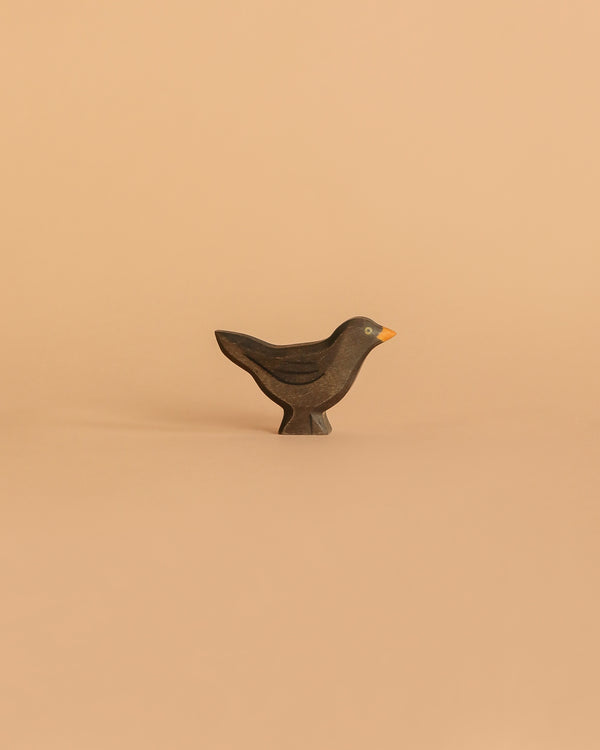 The Handmade Holzwald Blackbird is a small, dark wooden bird figurine with a yellow beak on a light beige background—ideal for imaginative play and a charming, eco-friendly addition to any sustainable toy collection.
