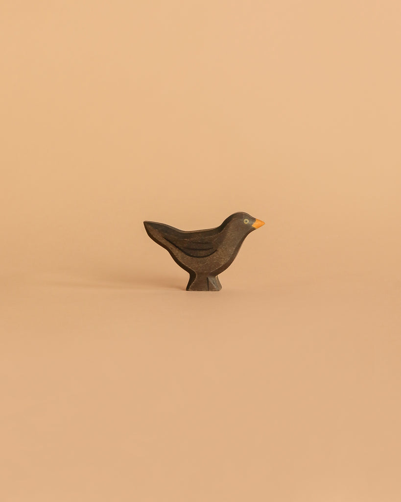 The Handmade Holzwald Blackbird is a small, dark wooden bird figurine with a yellow beak on a light beige background—ideal for imaginative play and a charming, eco-friendly addition to any sustainable toy collection.